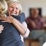 An older woman smiles as a younger woman visits her and hugs her, showing the effect that acts of kindness can have on senior loved ones.