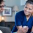 A nurse smiles as she helps an older couple with their medication in the comfort of their own home, showing the benefits of in-home nursing services.