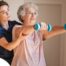 A physical therapist helps an older patient lift weights, representing how home health professionals can help with the hospital to home transition and the recovery that it entails.