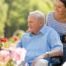 A caregiver brings an older adult with a wheelchair to see some flowers representing how professional caregivers can make outdoor activities accessible.