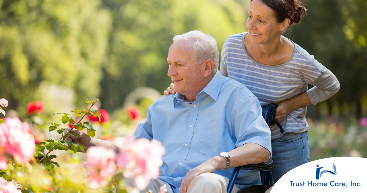 A caregiver brings an older adult with a wheelchair to see some flowers representing how professional caregivers can make outdoor activities accessible.